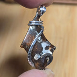 Metallic pendant held between fingers against a wooden background