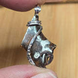 Hand holding a unique silver pendant with a textured design against a blurred background