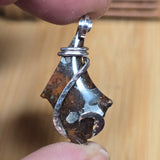 Metallic pendant held between two fingers against a wooden background