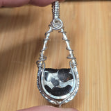 Silver wire-wrapped pendant with a central stone on a wooden surface