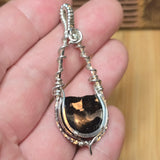 Silver pendant with a Pallasite slice held in a hand against a wooden background