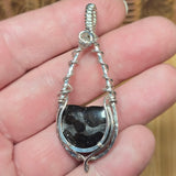 Silver wire-wrapped pendant with a Pallasite stone held in a hand.