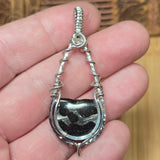Silver pendant with Pallasite stone held in a hand against a wooden background