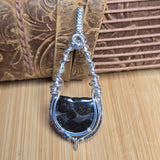 Silver pendant with a Pallasite stone on a textured wooden surface