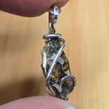 Close-up of a silver pendant with embedded stones held between fingers against a blurred background