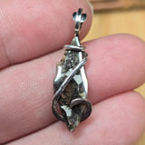Silver pendant held between fingers with a blurred background