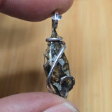 Close-up of a silver pendant held between fingers with a blurred wooden background