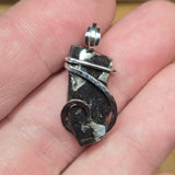 Silver pendant held between fingers on a light skin background
