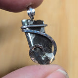Silver pendant held between fingers against a blurred background