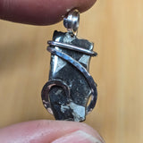 Close-up of a silver pendant with a dark stone held between fingers against a blurred background