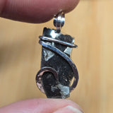 Black stone pendant with silver wire wrapping held between fingers against a blurred background