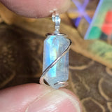 Silver pendant with a rainbow moonstone held between fingers against a blurred background