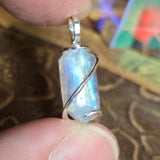 Silver pendant with a clear stone held between fingers on a patterned surface