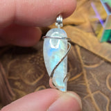 Moonstone pendant with silver wire wrapping held between fingers on a textured surface