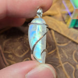 Rainbow Moonstone pendant with silver wire wrapping held between fingers against a textured background