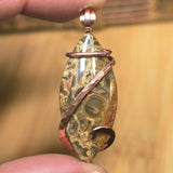 Hand holding a unique pendant with intricate design and copper wire wrapping against a blurred background