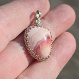 Pink marbled stone pendant with silver frame held in a hand