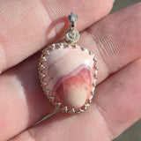 Pink marbled pendant with silver frame held between fingers