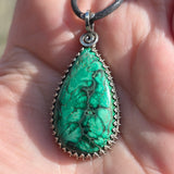 Teardrop-shaped green stone pendant on a leather cord held in a hand.