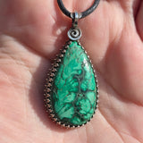 Plume Malachite pendant on a black cord held in hand