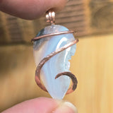 Jewelry pendant with a copper wire wrap held between fingers against a blurred background