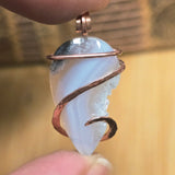 Pendant with a light purple stone and copper wire wrapping held by a hand against a blurred background