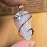 Crystal pendant with copper wire wrapping held between fingers against a blurred background