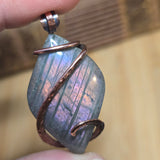 Close-up of a purple stone with copper wire wrapping held between fingers.