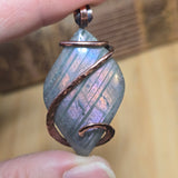 Jewelry with a stone and copper wire wrapping held between fingers against a blurred background