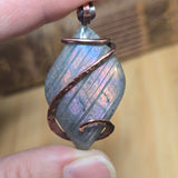 Close-up of a hand holding a crystal pendant with copper wire wrapping.