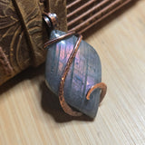 Copper and purple stone pendant on a wooden surface