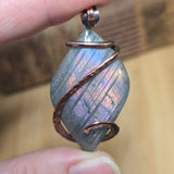 Crystal pendant with copper wire wrapping held between fingers against a blurred background