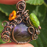 Close-up of a intricately designed pendant with a purple stone and decorative elements on a blurred green background.