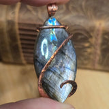 Labradorite pendant with copper wire wrapping held in hand against a blurred background
