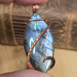 Labradorite pendant with copper wire wrapping held by a hand against a textured background