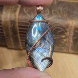 Labradorite pendant with copper wire wrapping held between fingers against a textured background