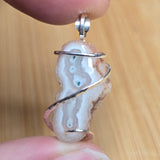 A close-up of a hand holding a silver spiral-wrapped geode pendant against a light wood background.