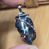 Decorative stone pendant with copper wire wrapping held between fingers on a wooden surface