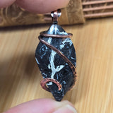 Marble-patterned pendant with copper wire wrapping held between fingers on a wooden surface