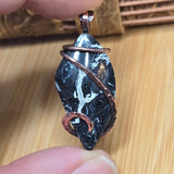 Hand holding a marbled stone pendant with copper wire wrapping on a wooden surface