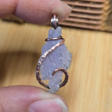 Hand holding a pendant with a copper wire wrap design on a wooden surface