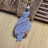 Decorative stone pendant with copper wire wrapping on a wooden surface
