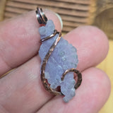 Hand holding a crystal pendant with copper wire wrapping