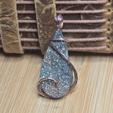 Teardrop-shaped pendant with glittery surface and copper wire wrapping on a textured background