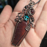 Red moss agate coffin pendant with antiqued copper wirework, garnet accents and an iridescent green skull.