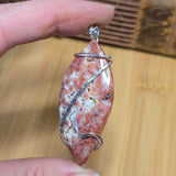 Hand holding a stone pendant with wire wrapping on a wooden surface