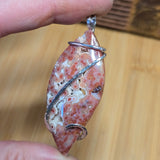 Hand holding a pendant with a natural stone design on a wooden surface