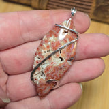 Hand holding a stone pendant with silver accents on a wooden surface