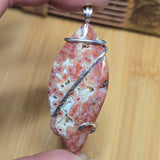 Pendant with a natural stone design held by a hand on a wooden surface