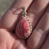 Pink stone pendant with sterling silver setting held in a hand